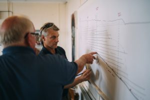 Two men discussing information on a whiteboard